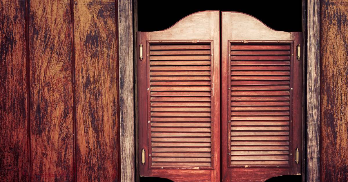 A close-up of wooden swinging saloon doors in a doorway. There is wood paneling on either side of the door.